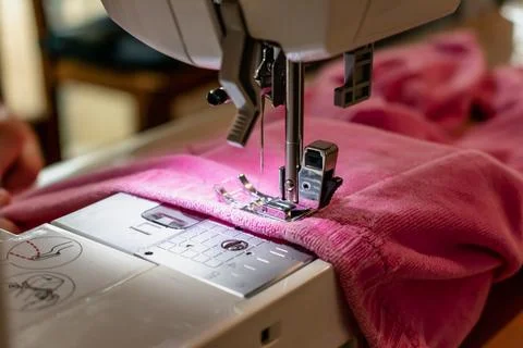 Man using a sewing machine with a pink garment, for repair work, customizat.. Foto stock