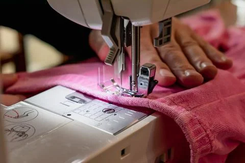 Man using a sewing machine with a pink garment, for repair work, customizat.. 库存照片