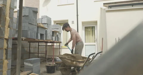 Man using shovel and wheelbarrow on a building site Stock Footage 246382278