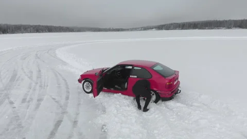 Man using shovel to dig out his red car from snowbank at ice race track Vidéo 145876302