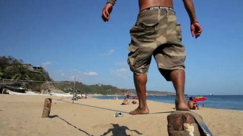 Man using a slackline in the beach, her shadow projected in the sand. Video stock 49763355