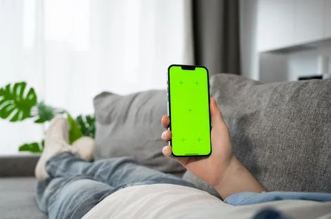 Man using smarphone with green screen lying on the couch at home. Modern Stock Photos