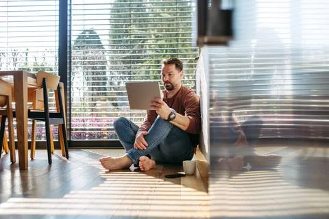 Man using smart home app working on tablet and sitting on floor. Stock Photos