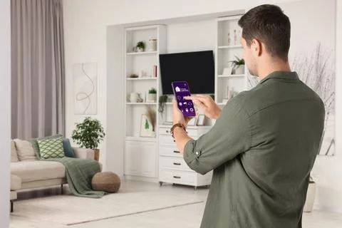 Man using smart home control system via application on mobile phone indoors Stock Photos