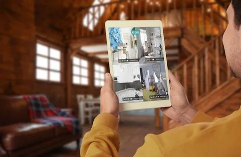 Man using smart home security system on tablet computer indoors, closeup. D.. Stock Photos