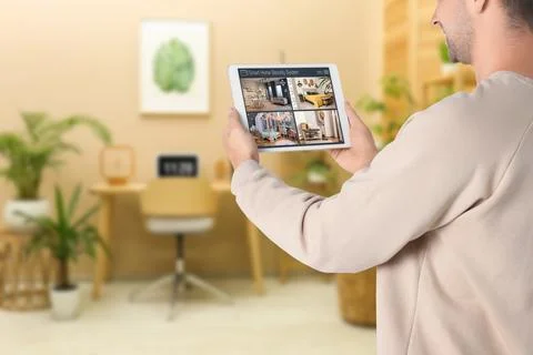 Man using smart home security system on tablet computer indoors, closeup. D.. Stock Photos