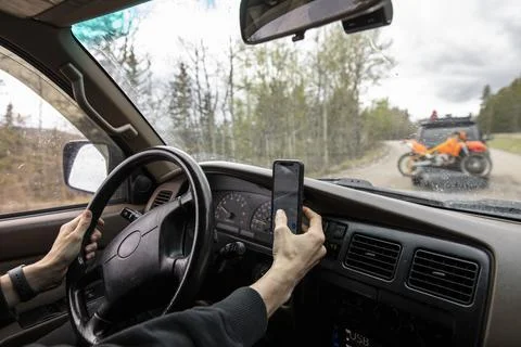 Man using smart phone driving overland SUV on remote road in woods Stock Photos