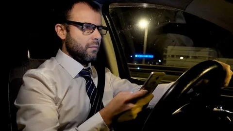 Man using a smart phone while driving a car on the road at night city . Young 库存影片 82638327