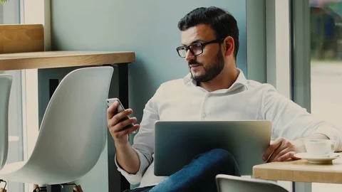 Man using smartphone and holding his laptop on the legs inside the cafe Stock Footage 112989690