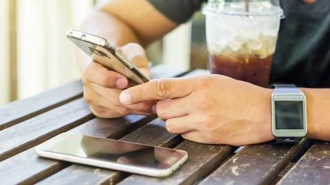 Man using a smartphone and a smartwatch in a coffee shop. Stock Photos