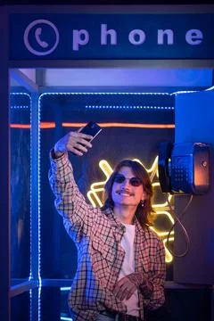 Man using smartphone and take selfie in old phone box at night with neon light Stock Photos