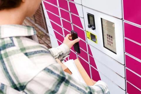 Man using a smartphone at an automated parcel locker to pick up packages. F.. Stock Photos