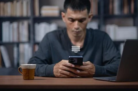 Man using smartphone at desk with bookshelf background in modern office setti Stock Photos