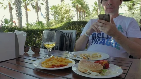 A man using a smartphone, drinking beer and eating a burger with French fries. A Stock Footage 82417560