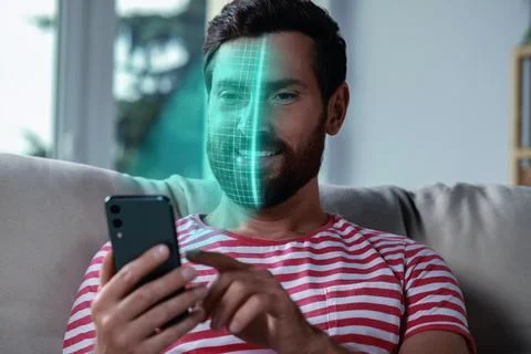 Man using smartphone with facial recognition system at home. Security appli.. Stock Photos