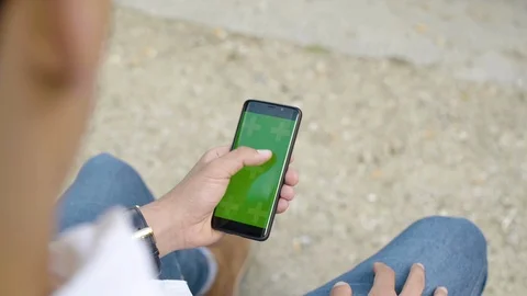 Man using smartphone with Green Screen Sitting on bench in park, Swiping Stock Footage 111927171