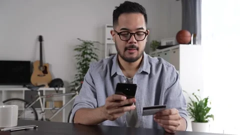 Man using smartphone holding credit card for online shopping and payment at home Stock Footage 167940698