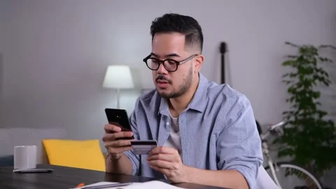 Man using smartphone holding credit card for online shopping and payment at home Stock Footage 167942631
