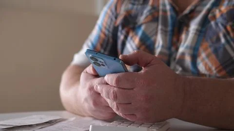 Man using smartphone indoors while sitting at table with keyboard and documents Stock Photos