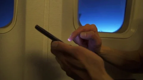 Man using a smartphone inside an airplane next to a window. Stock Footage 76491169