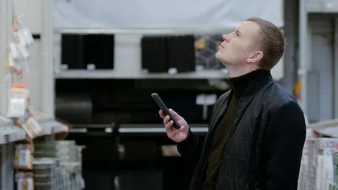 Man using smartphone to locate items on top shelves in hardware store. A man in 스톡 사진