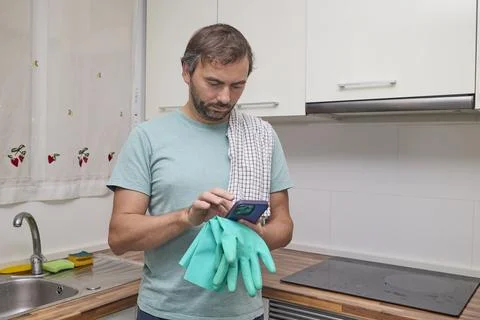 Man using smartphone in modern kitchen holding rubber gloves Stock Photos