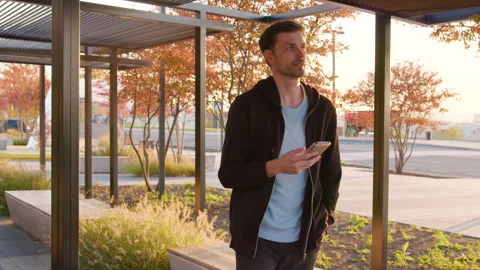 Man using smartphone in modern urban setting, surrounded by greenery and Stock Footage 317702828