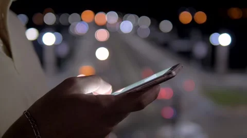 Man using smartphone at night with city traffic lights in background Stock Footage 303293544