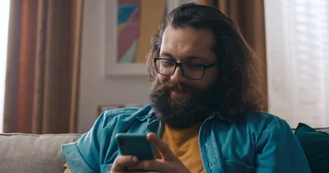 A man using a smartphone, sitting on the couch at home, a young guy staring at 库存影片 218182268