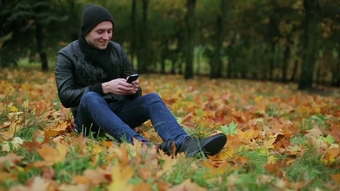 Man using smartphone sms chatting in park in autumn Stock Footage 73907918