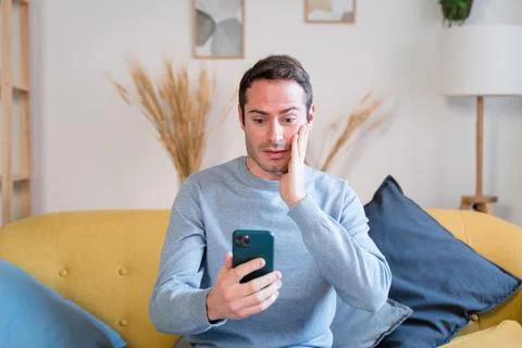 Man using smartphone on sofa at home is in shock because news Stock Photos