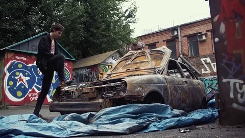 Man using smartphone standing on fender of crashed burned car. Urban lifestyle Stock Footage 80008726