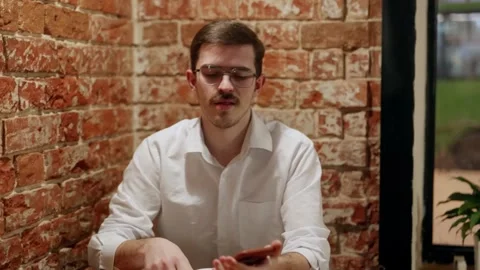 Man using smartphone at table with brick wall 스톡 동영상 342779602