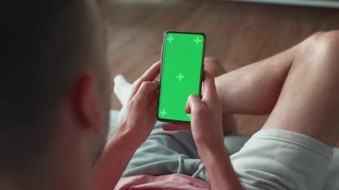 Man Using Smartphone in vertical Mode with Green Mock-up Screen, Doing Swiping 스톡 동영상 241746044