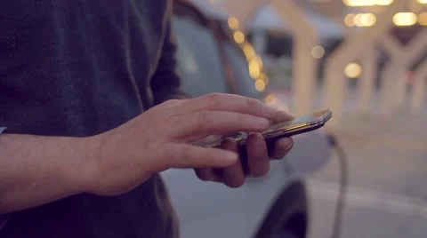 Man using the smartphone while charging its electric car Stock Footage 62226450