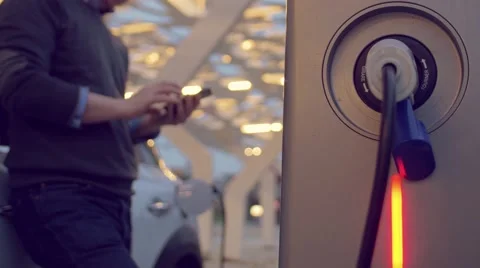 Man using the smartphone while charging its electric car Stock Footage 62226478