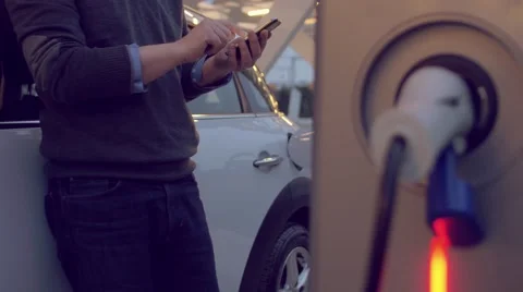 Man using the smartphone while charging its electric car Stock Footage