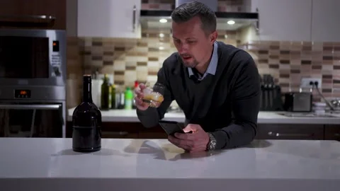 Man Using Smartphone While Drinking Whiskey in Modern Kitchen. A man in a s.. Video stock 332416046