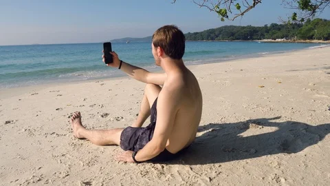 Man Using Smartphone While Sitting on Beautiful Sandy Beach Stock Footage 119691831