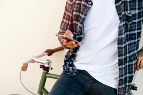 Man using a smartphone while sitting on bike outdoors. Stock Photos