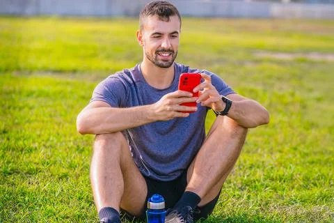 Man using smartphone while sitting on grass in outdoor park Stock-Fotos
