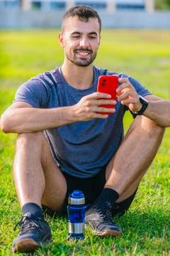 Man using smartphone while sitting on grass in outdoor park Foto stock