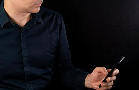 Man using smartphone while sitting against dark background in modern setting Stock Photos