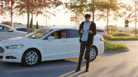 Man using smartphone while standing next to a white car in a modern urban Stock Footage 316835730