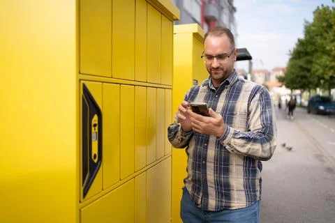 Man using smartphone while standing near bright yellow delivery lockers in an Stock Photos