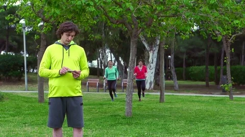 Man using smartphone while women jogging, steadycam shot, slow motion shot Stock Footage 71830221