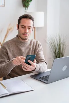 Man using smartphone while working on laptop at home Stock Photos