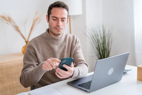 Man using smartphone while working on laptop at home Stock Photos