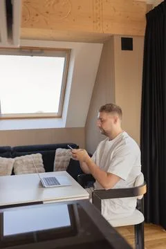 Man using smartphone while working with laptop at home office. Concept of remote Stock Photos