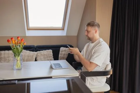 Man using smartphone while working with laptop at home office. Concept of remote Stock Photos